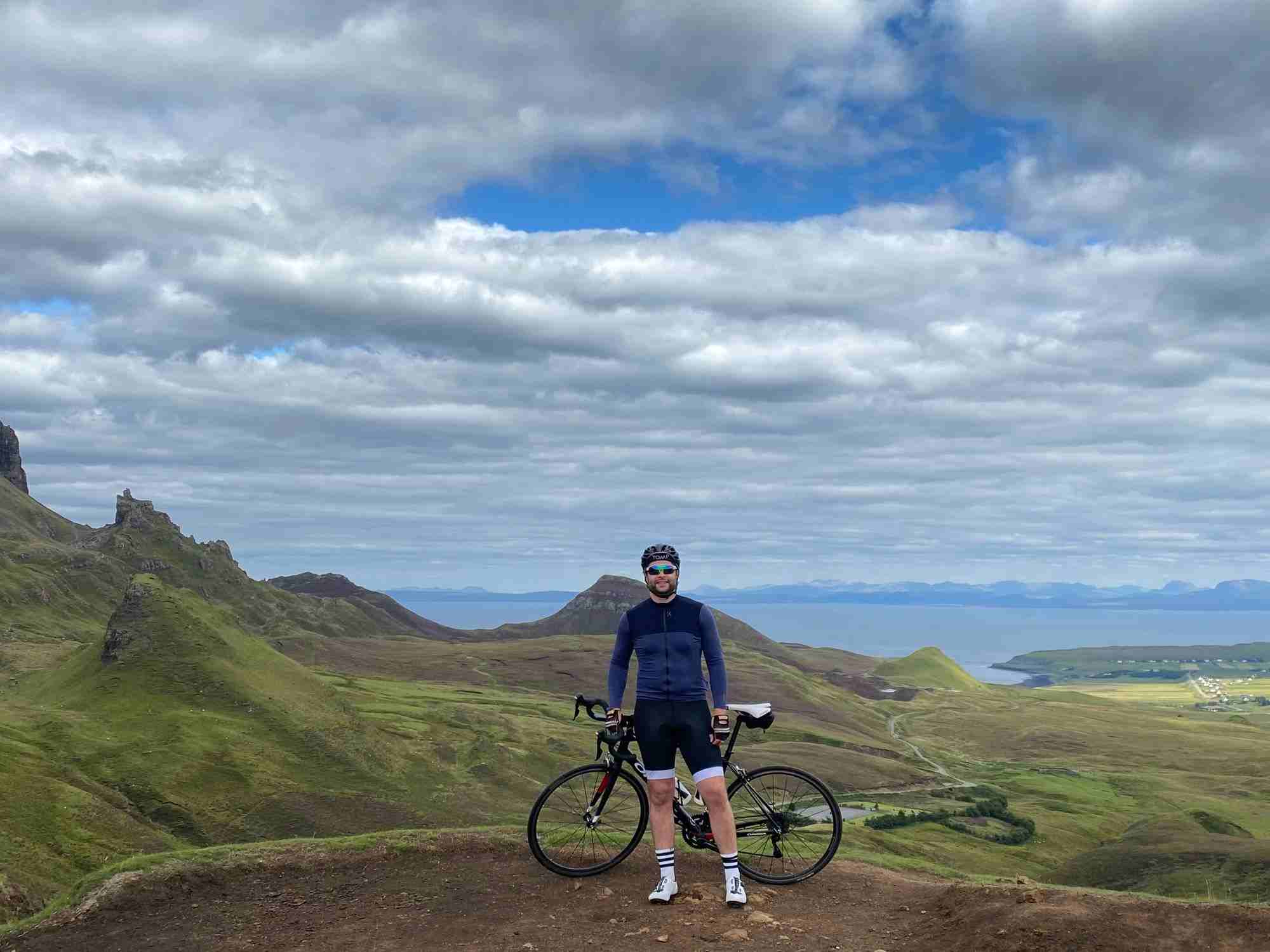 Cyclist-Standing-With-Bike-With-Green-Rolling-Hills-In-Background